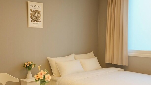Une chambre d’hôtel avec un lit, une table ronde blanche, deux chaises blanches, un vase avec des fleurs et un tableau encadré au mur.