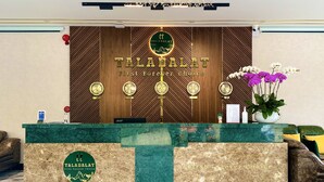 A reception desk with a wooden backdrop, a chandelier, and a sign that reads "TALADALAT First Forever Choice". - Tala Dalat Hotel (Xuan Huong - Da Lat)