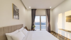 A hotel room with a large bed, a bedside table, a TV, and a view of the mountains through the balcony doors. - Tala Dalat Hotel (Xuan Huong - Da Lat)