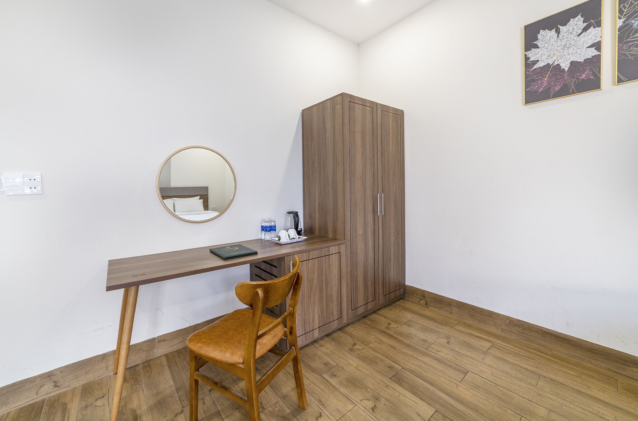 Una habitación con un escritorio de madera, una silla, un armario, un espejo y un cuadro en la pared.