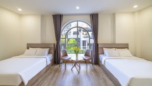 A hotel room with two beds, a small table with chairs, and a large arched window with curtains. - Tala Dalat Hotel (Xuan Huong - Da Lat)