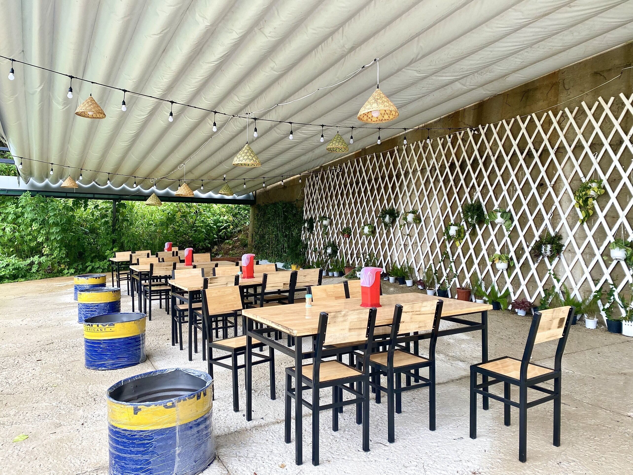 An outdoor dining area with tables and chairs, string lights, and potted plants.