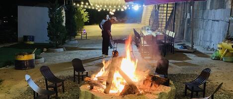 An outdoor seating area with a fire pit surrounded by chairs, under a marquee with string lights.