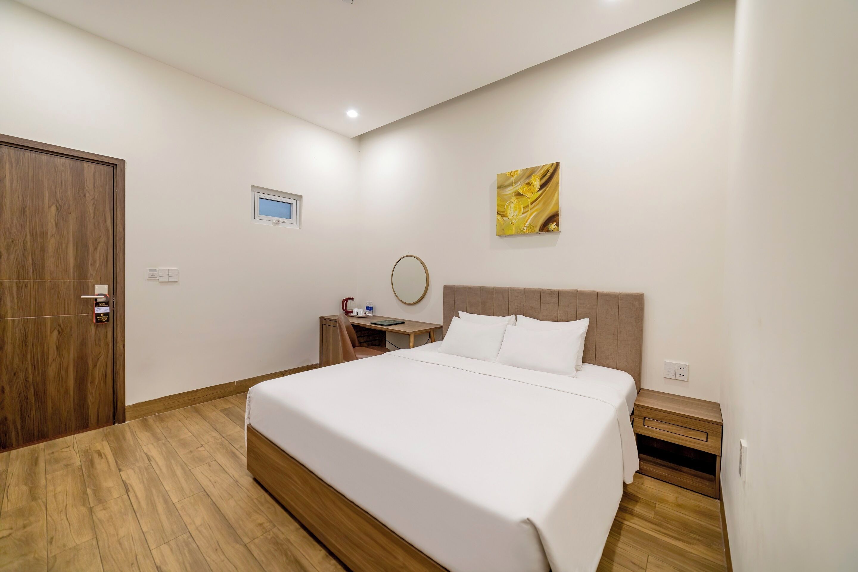 Un dormitorio ordenado con una cama grande, mesitas de noche, un armario de madera y un pequeño escritorio con silla.