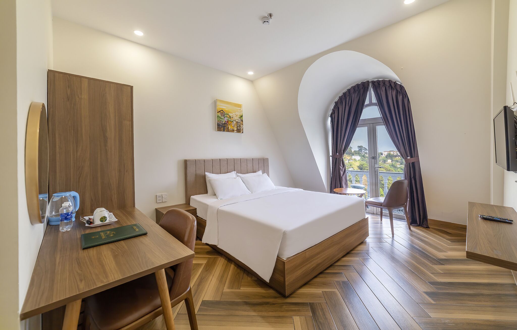 Habitación de hotel con cama, escritorio, silla, televisor y ventana con cortinas.