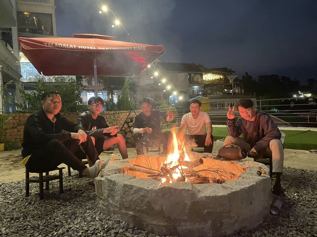 Un grupo de personas sentadas alrededor de una hoguera en un hotel, con zona de estar al aire libre.