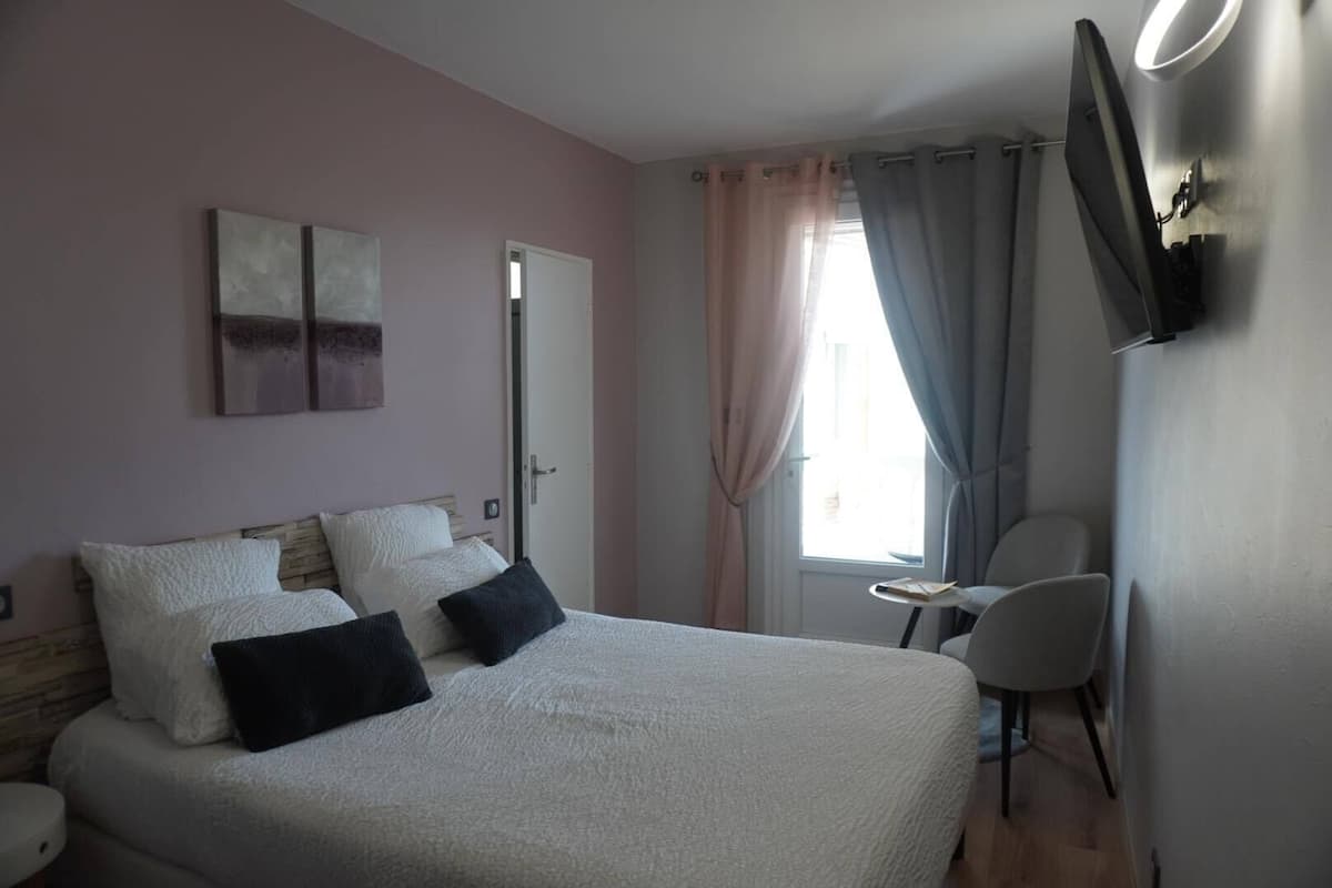 A bedroom with a bed, a chair, a desk, and a TV on the wall.