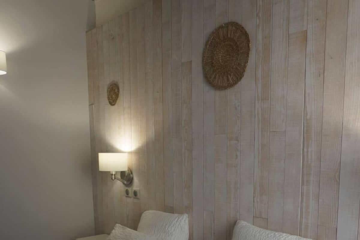 A bedroom with two beds, a nightstand, a wall-mounted lamp, and decorative wall art.