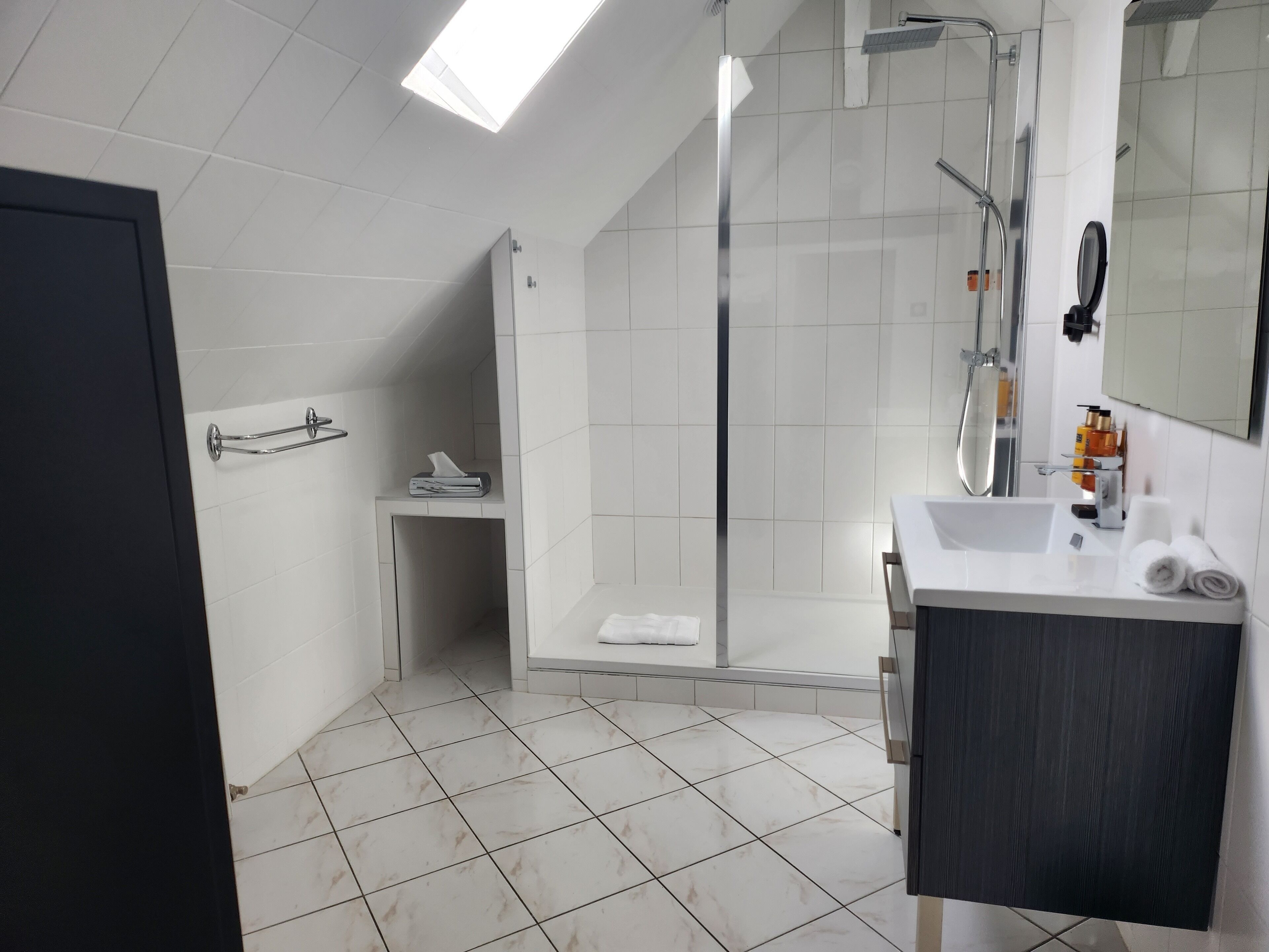 Un baño moderno con cabina de ducha, lavabo con artículos de aseo y espejo.