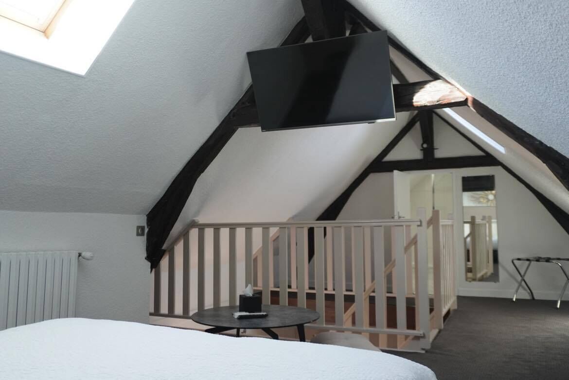 A bedroom with a sloped ceiling, a bed, a small table, and a TV mounted on the ceiling.