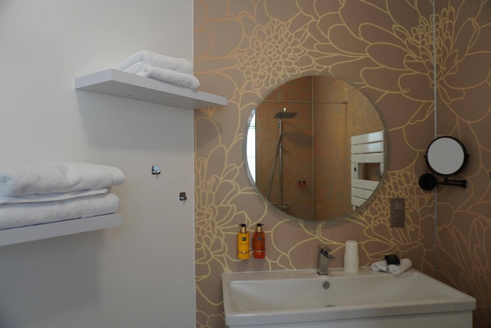 A bathroom with a white sink, a round mirror, a towel rack, and a shower.