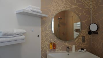 A bathroom with a white sink, a round mirror, a towel rack, and a shower.