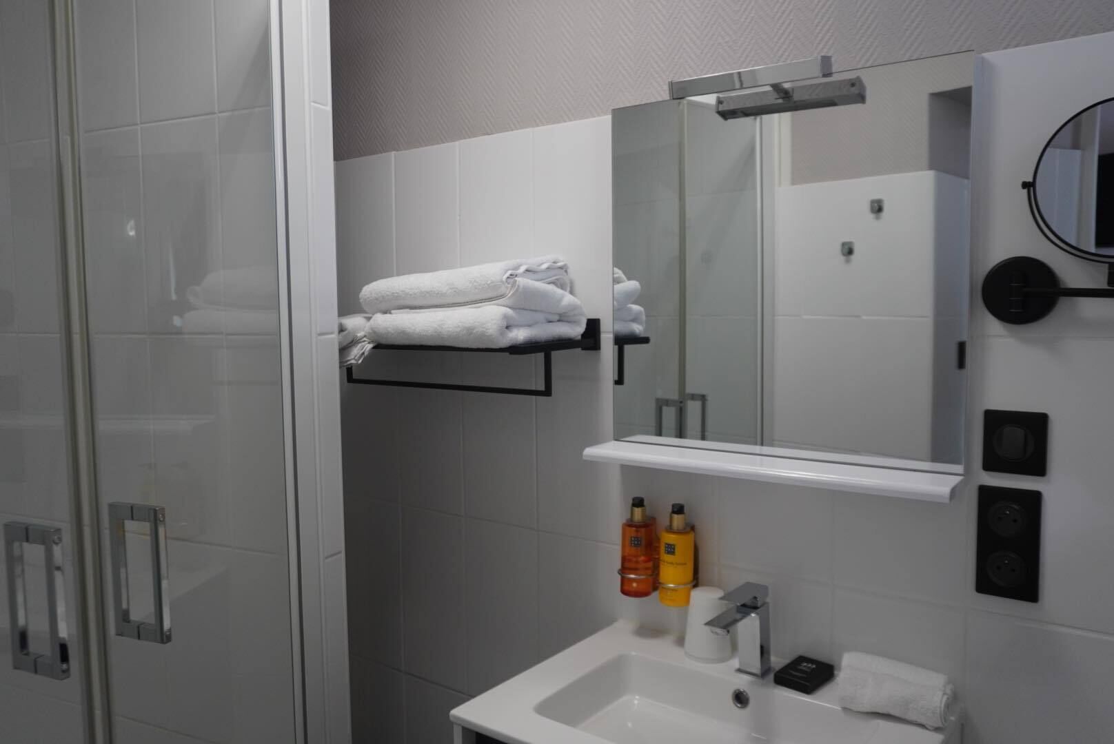 Un bany modern amb plat de dutxa de vidre, un envàs de color blanc i un mirall a la part superior, i un porta tovalloles amb tovalloles netejades.