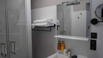 Un bany modern amb plat de dutxa de vidre, un envàs de color blanc i un mirall a la part superior, i un porta tovalloles amb tovalloles netejades.