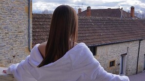 A person in a white robe standing on a balcony with a stone building in the background. - Hôtel Villa Pona (Digoin)
