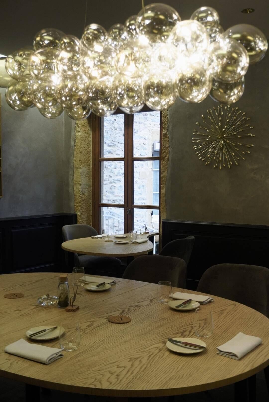 A round dining table with plates, glasses, and cutlery. There is a chandelier above the table.