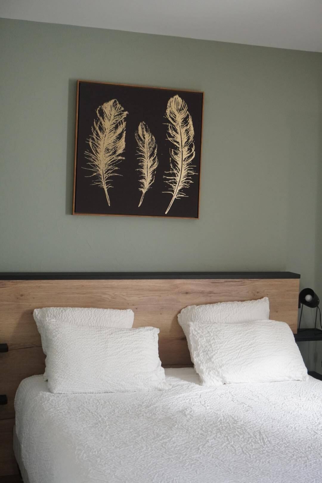 Une chambre à coucher avec un lit, deux oreillers et une œuvre d’art encadrée représentant des plumes, accrochée au mur.