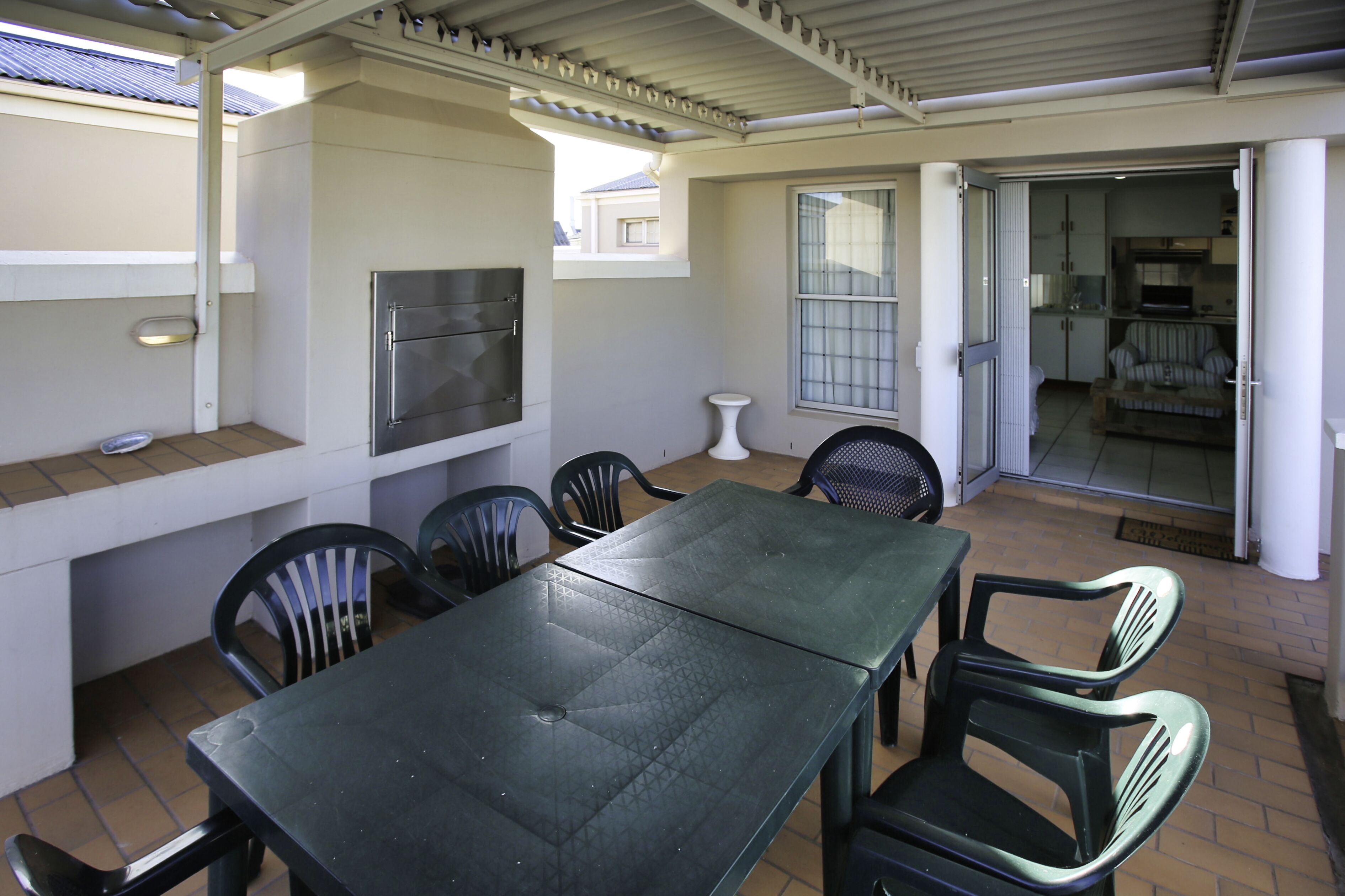 Un espace extérieur aménagé en terrasse, avec une table et des chaises, un barbecue et une vue sur l’immeuble voisin.