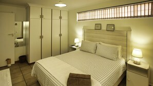 A bedroom with a large bed, a nightstand with a lamp, a wardrobe, and a window with blinds. - Top Deck Langebaan 6-sleeper (Langebaan)