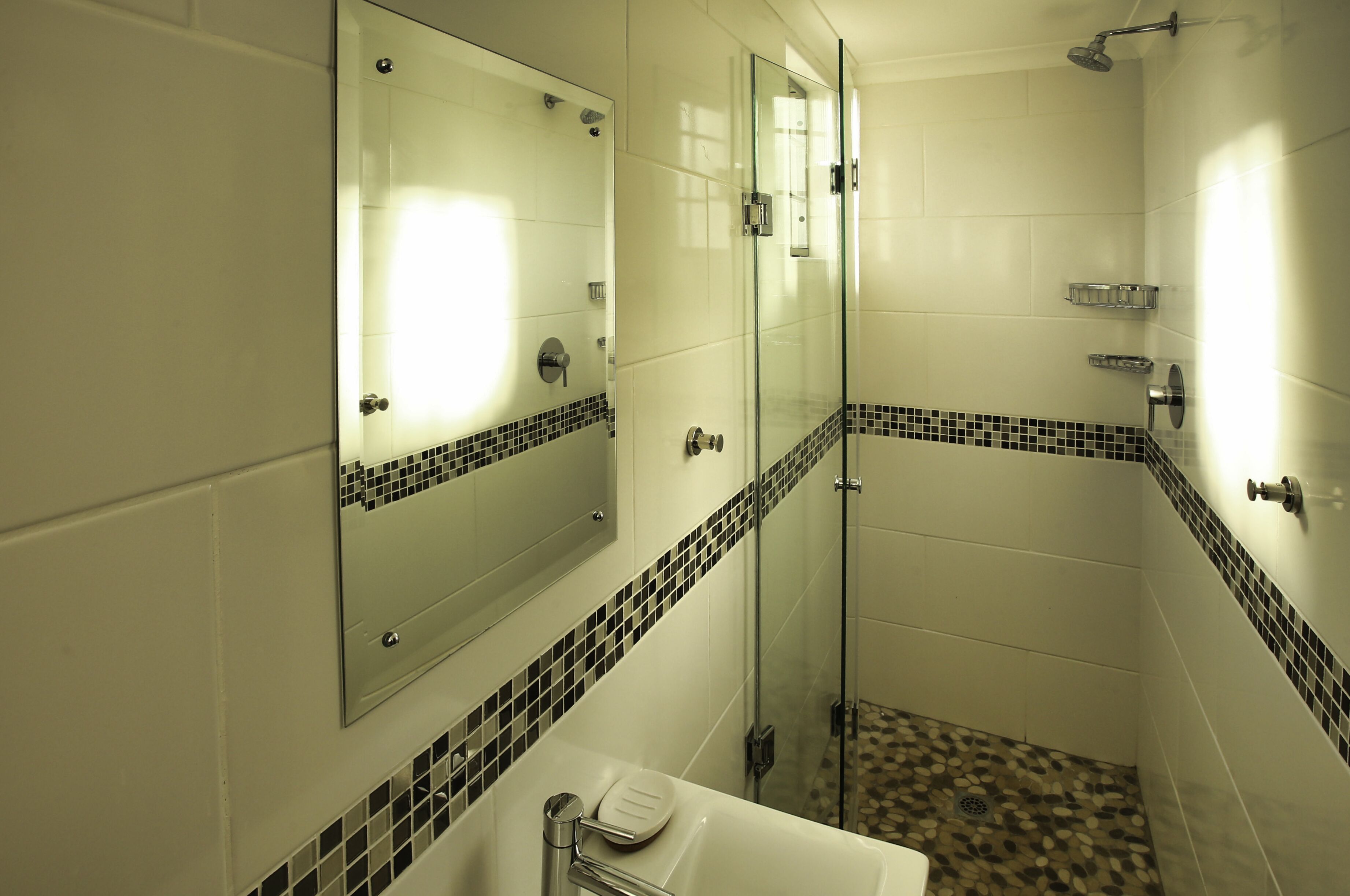A modern bathroom with a glass-enclosed shower, a large mirror, and a tiled floor.