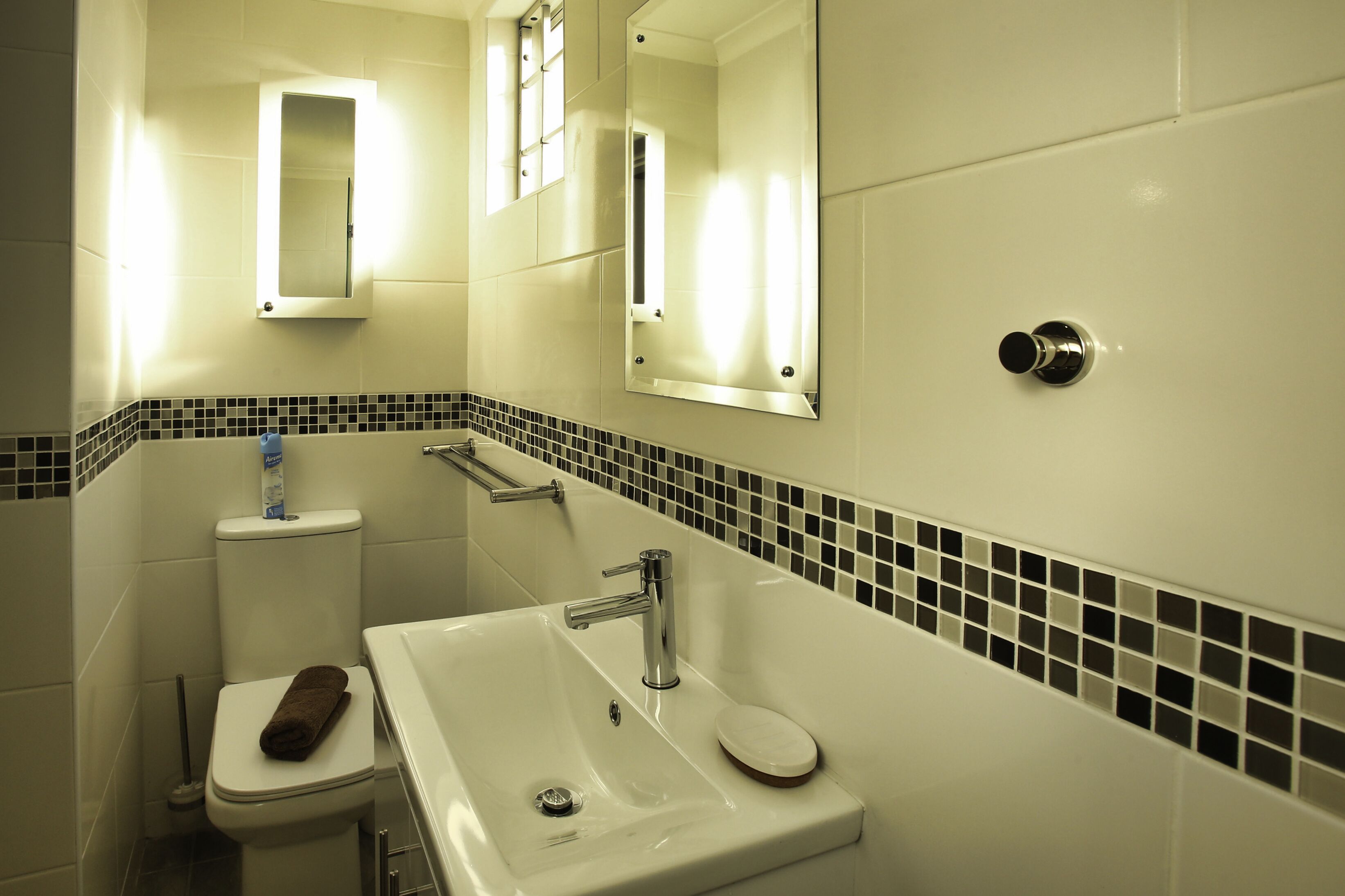 A bathroom with a white sink, a mirror, a toilet, and a towel on the toilet.