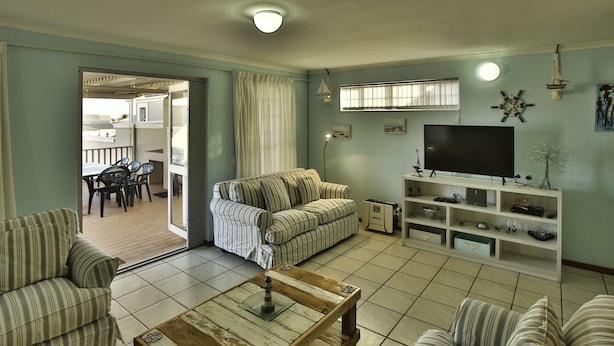 A living room with a sofa, armchairs, a coffee table, a TV, and a shelf with decorative items. - Top Deck Langebaan 6-sleeper (Langebaan)