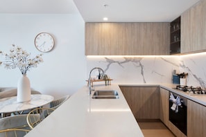 A modern kitchen with a central island, wooden cabinets, a marble backsplash, and a wall-mounted clock.