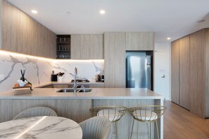 A modern kitchen with a marble backsplash, stainless steel appliances, and a built-in island with bar stools. - Magnificent Full Ocean View at Casino Free Parking (Broadbeach)