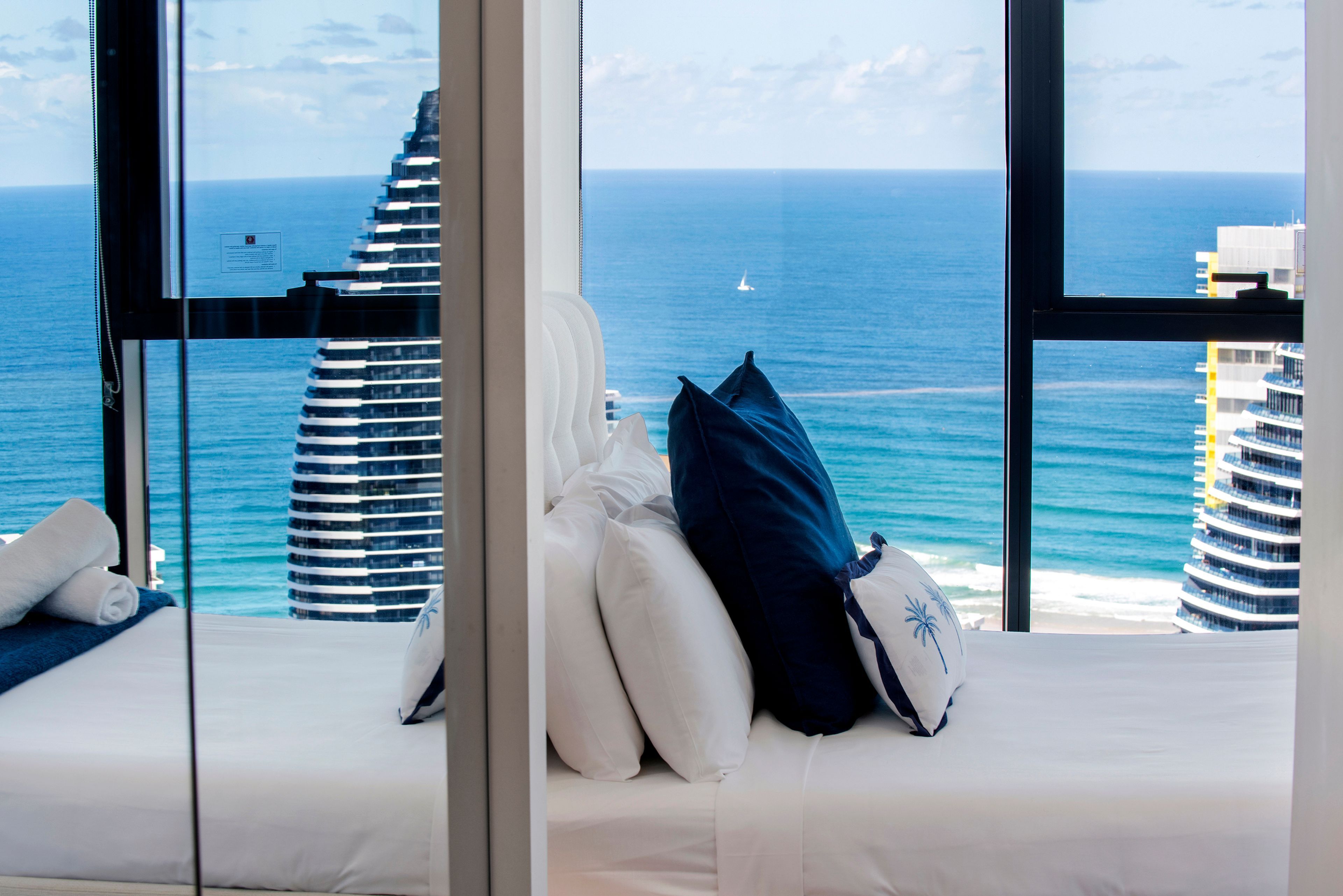 Ein Hotelzimmer mit Bett, Kissen und Blick auf das Meer und die Gebäude.