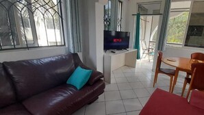 A living room with a brown leather sofa, a red armchair, a wooden dining table with chairs, and a TV displaying 'NETFLIX'. - Lux Suites Royal Palms Apartments Mtwapa (Mtwapa)