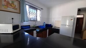 A kitchen with a microwave, sink, blue storage bins, a refrigerator, and a window with a curtain. - Lux Suites Royal Palms Apartments Mtwapa (Mtwapa)