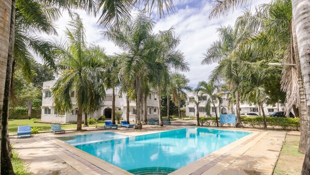 A swimming pool surrounded by palm trees and a building with multiple windows. - Lux Suites Royal Palms Apartments Mtwapa (Mtwapa)
