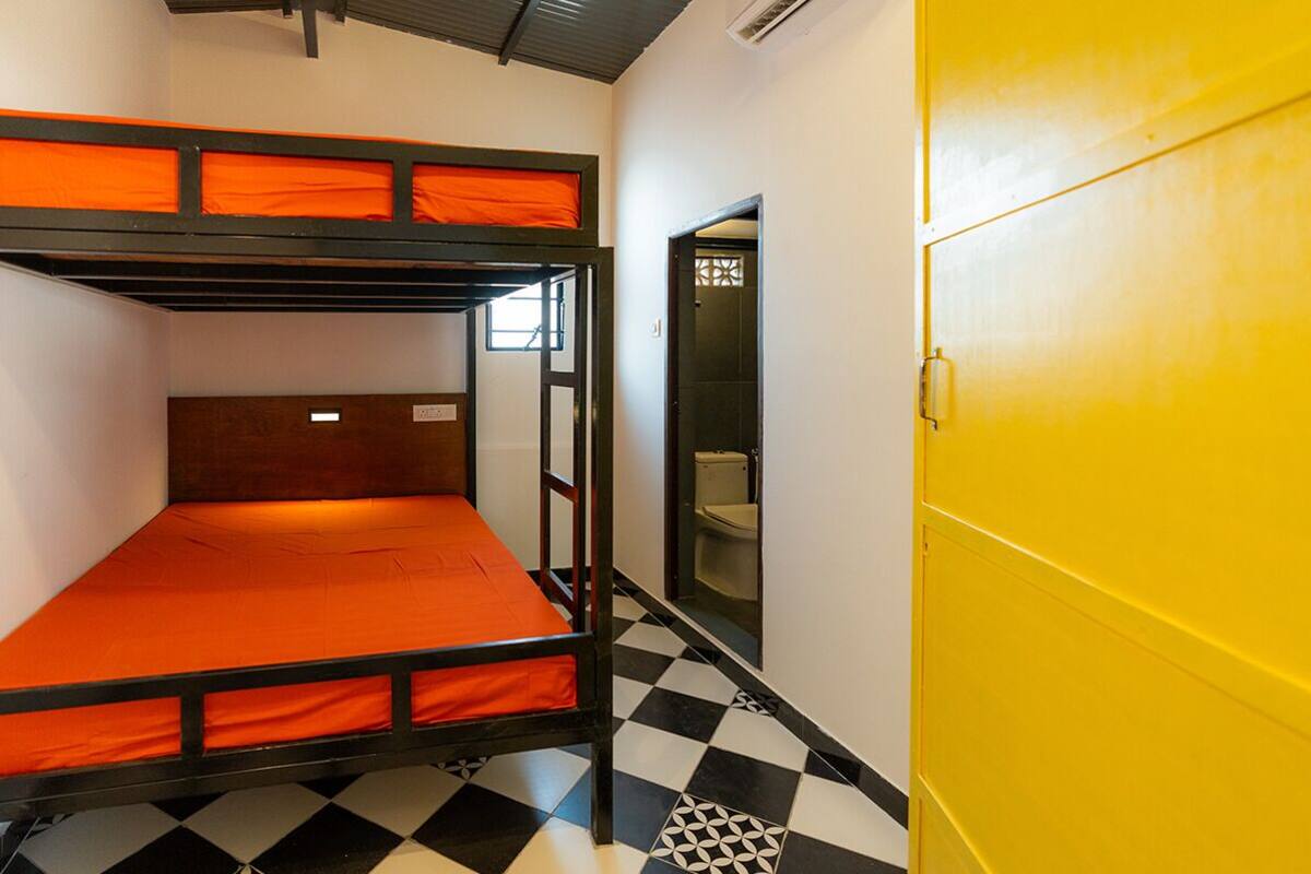 A bunk bed room with a checkered floor, a yellow door, and a visible toilet in the adjacent room.