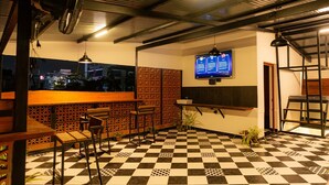Pavimento a scacchi, zona bar, posti a sedere e uno schermo televisivo.