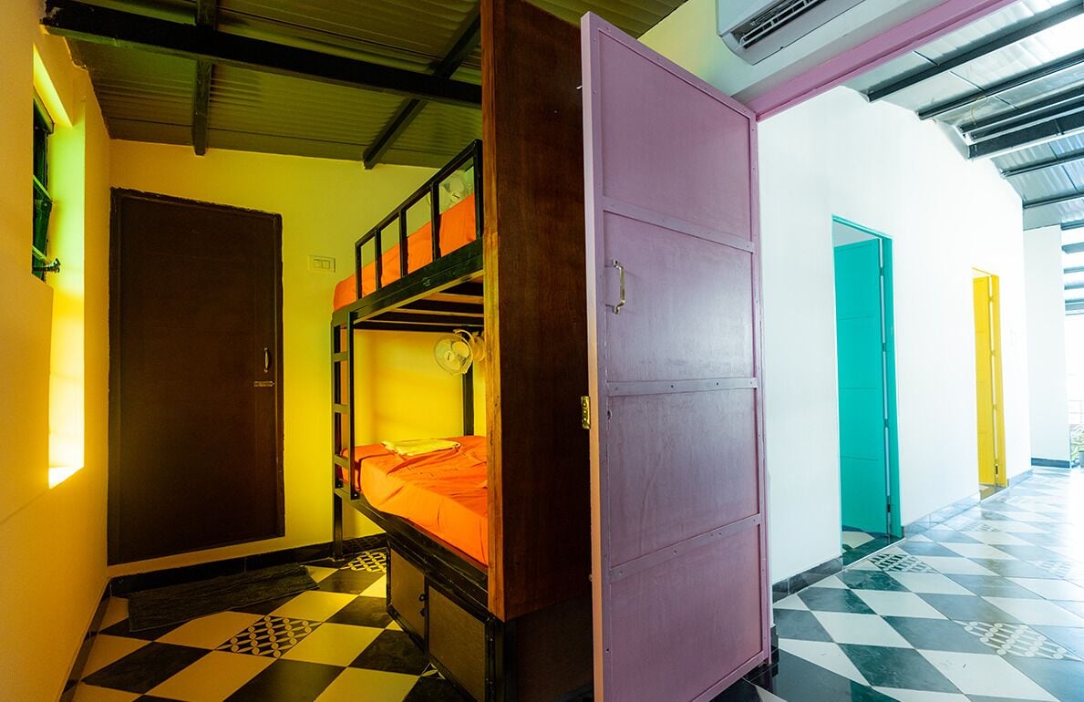 A dormitory room with bunk beds, a purple wardrobe, and a checkered floor.