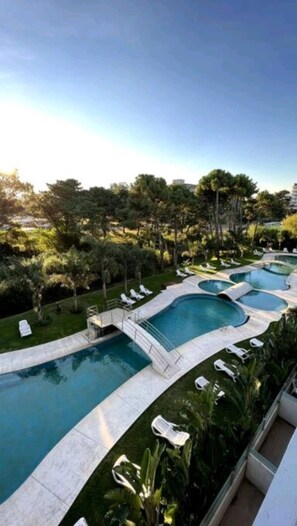 A pool area with multiple swimming pools, lounge chairs, and surrounding greenery. - Departamento 3 Ambientes 2 Baños Pinamar Centro (Pinamar)