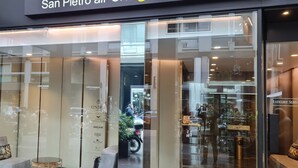 Une entrée d’hôtel moderne avec des portes en verre, un espace détente avec un canapé et une petite table, et une enseigne indiquant « San Pietro al Lago ».