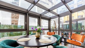 Une pièce baignée de lumière, avec une table ronde, des chaises vertes et un vase rempli de fleurs.