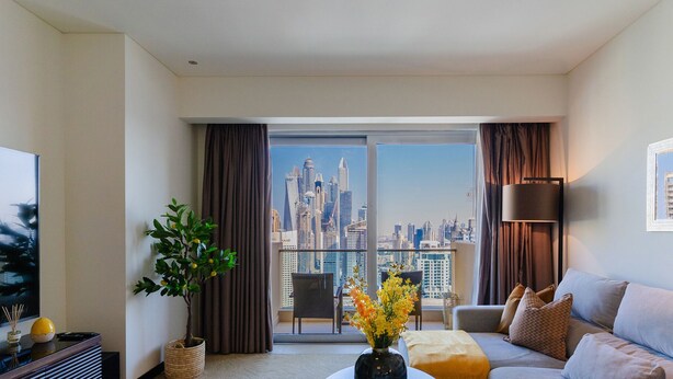 A modern living room with a city skyline view, a sofa, a coffee table, and a potted plant. - Stylish 1BR unit Address Marina (Dubai)