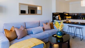 A modern living room with a sofa, coffee table, and a kitchen area in the background. - Stylish 1BR unit Address Marina (Dubai)
