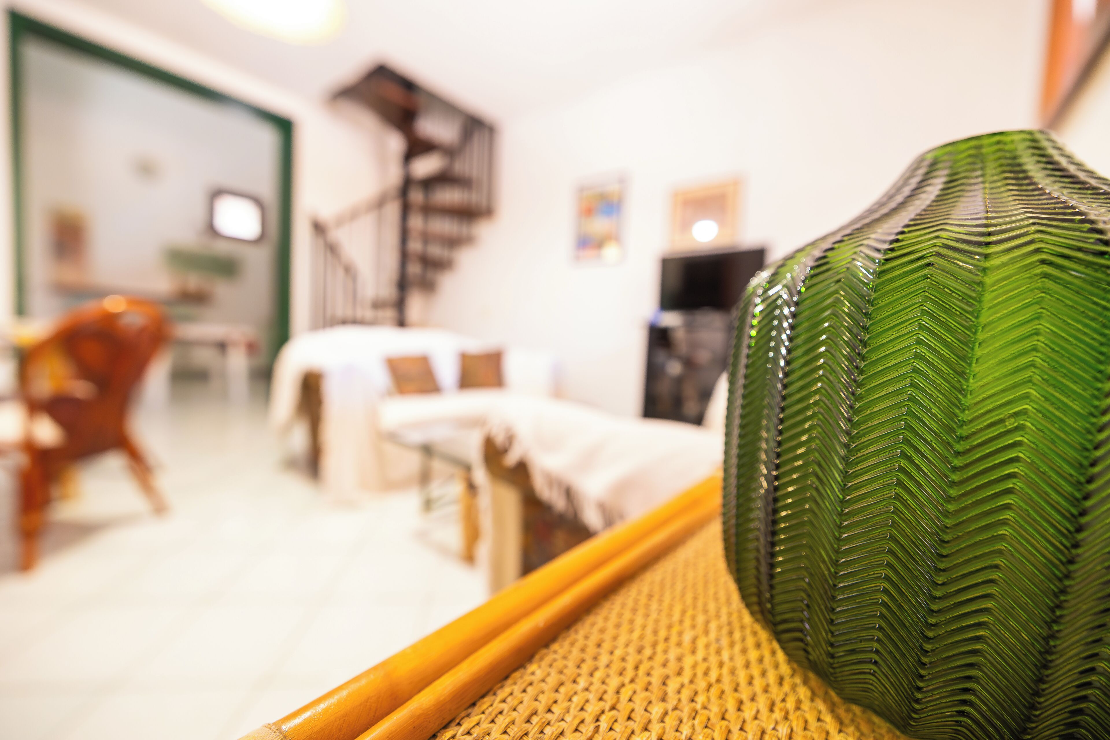Um quarto com uma cama, uma cadeira, uma escada e um vaso verde sobre uma mesa.