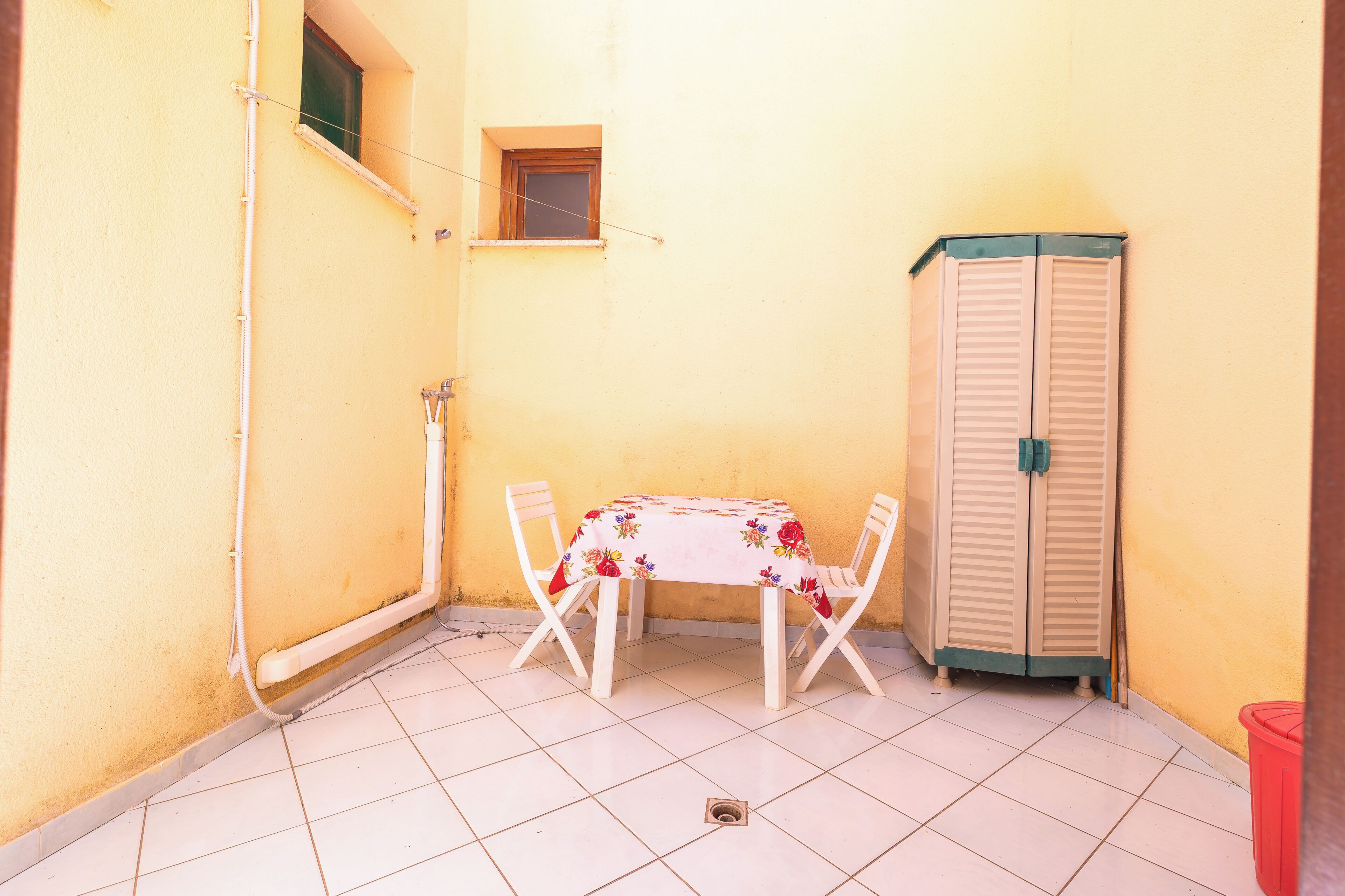 Une petite terrasse extérieure avec une table et des chaises, un meuble de rangement et une fenêtre.