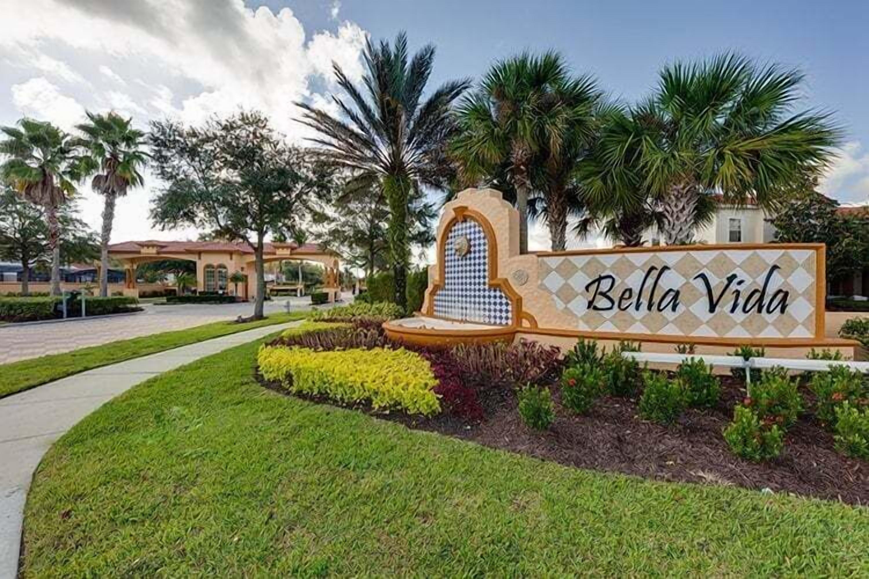 A sign for 'Bella Vida' with a decorative archway, surrounded by well-maintained landscaping and palm trees.