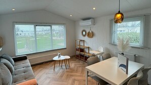 Un salon moderne avec un canapé, une table à manger et des chaises. On y trouve une fenêtre avec des stores, un appareil de climatisation et un luminaire suspendu.