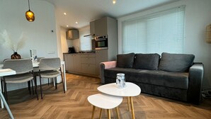 Un salon moderne avec un canapé gris, deux petites tables rondes blanches et un parquet en bois à motifs chevrons.