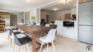 A modern kitchen with a wooden table and chairs, a refrigerator, and a coffee machine.