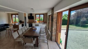 A spacious living area with a dining table, chairs, a sofa, and a kitchen area with a TV and windows.