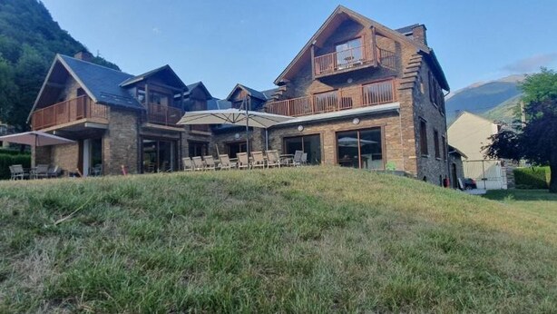 A large, multi-story building with a stone facade, multiple balconies, and a covered outdoor seating area.