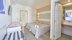 A hotel room with a bed, a desk, a chair, a bedside table, a mirror, and a bathroom with a sink and mirror. - AHOI! Urban Beach Hotel (Palma de Mallorca)