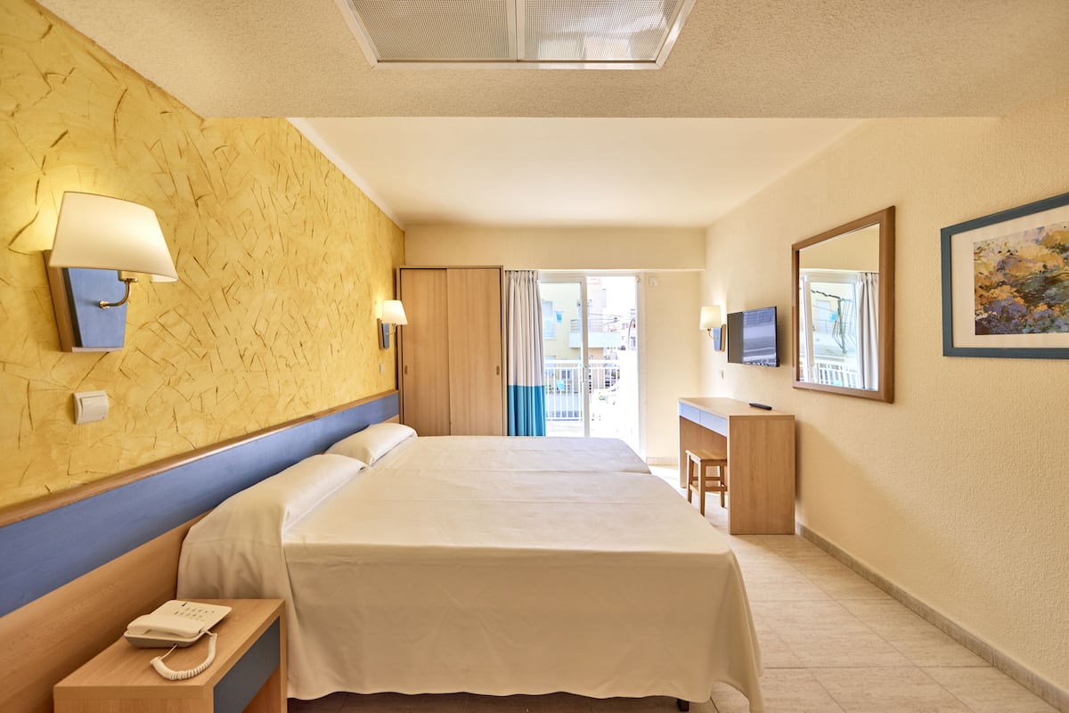 Hotellihuone, jossa on suuri sänky, yöpöydällä lamput, työpöytä, jossa on televisio, ja näkymä ovesta.